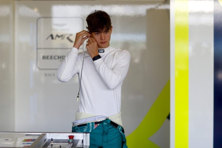 Young race car driver in white racing suit adjusting earpiece at Grand Prix Racewear.