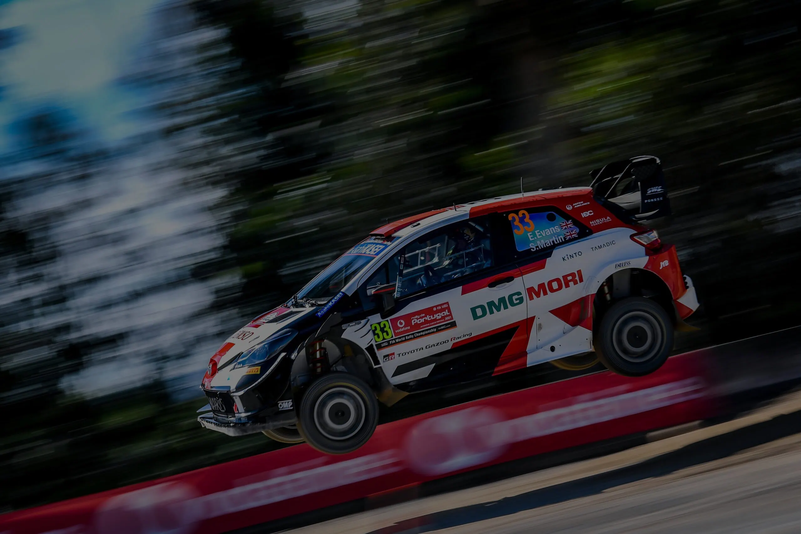 Rally car racing at high speed on a dirt track with motion blur background.