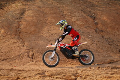 Young motocross rider in GPR Electric gear riding on dirt track with Grand Prix Racewear branding.