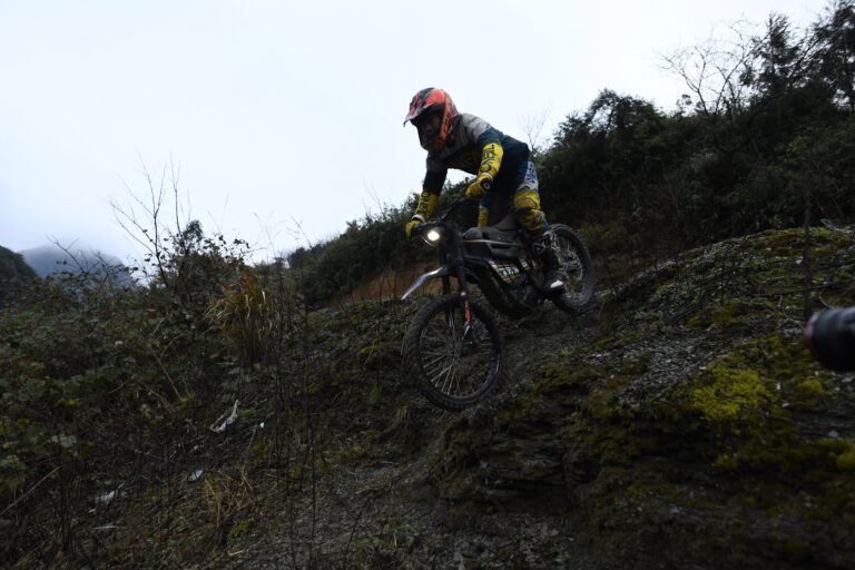 Motocross rider navigating a rocky, muddy trail on a mountain bike in outdoor terrain.
