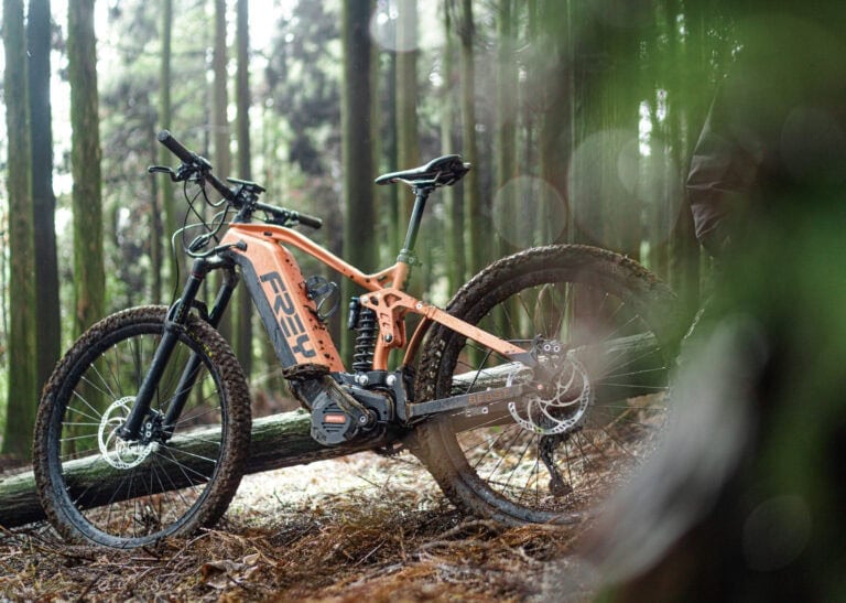 Electric mountain bike with full suspension and knobby tires on a forest trail, ideal for off-road cycling and adventure.