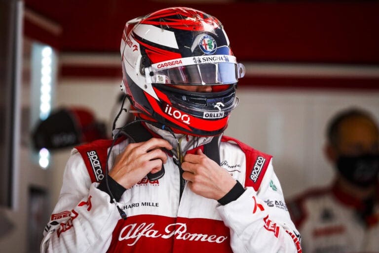 Formula 1 driver in Alfa Romeo racing suit and helmet preparing for a race, focused and ready in the garage.