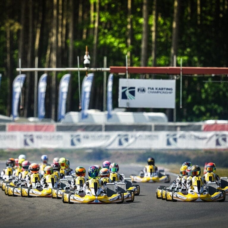Group of go-karts racing on a track with a forest background, showcasing Grand Prix Racewear for karting enthusiasts.