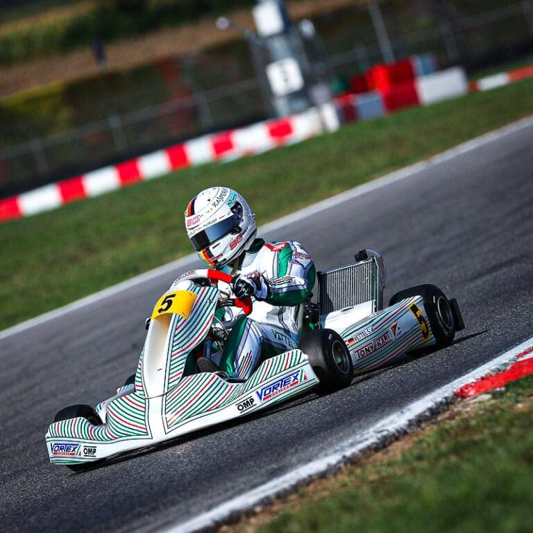 High-speed go-kart racing on a professional track with a driver in full racing gear and helmet, showcasing Grand Prix Racewear.