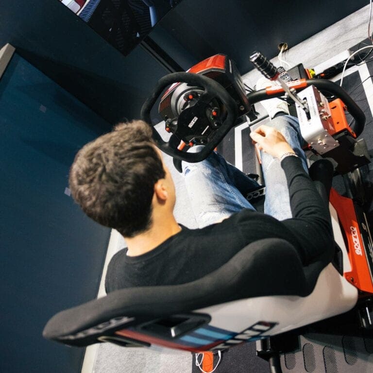 Young man racing simulator setup with steering wheel, pedals, and racing seat for immersive motorsport experience.