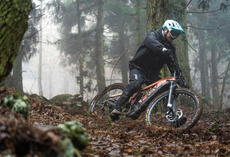 Mountain biker wearing a helmet and protective gear riding downhill on a forest trail.