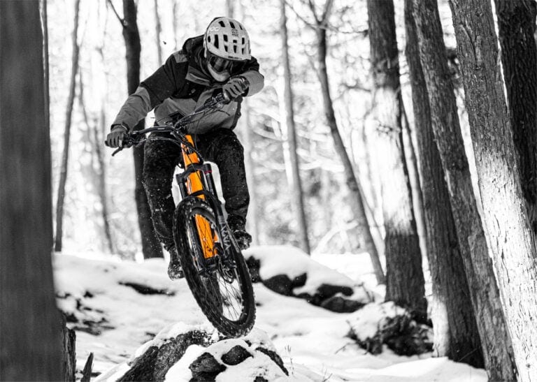 Mountain biker wearing a helmet riding through a snowy forest trail, showcasing off-road cycling gear and adventure.