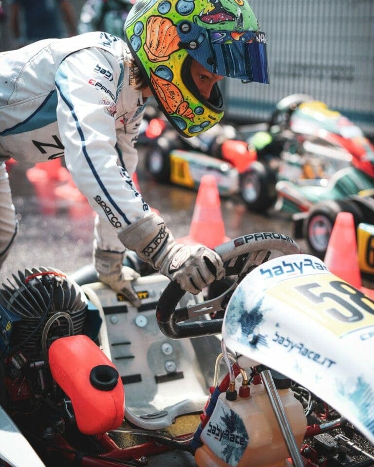 Kart racing driver in colourful helmet and racing suit preparing for race at Grand Prix Racewear event.