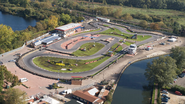 Aerial view of a go-kart racing track surrounded by greenery and water bodies, with race facilities and vehicles visible.