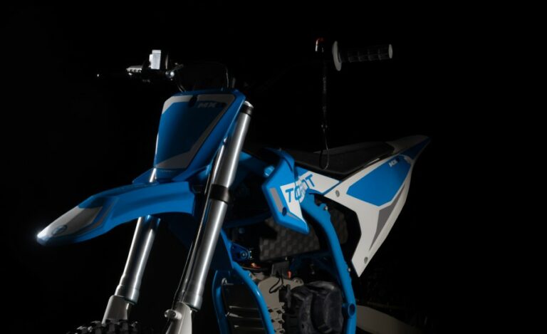 Close-up of a blue and white motocross bike with black background, highlighting the front suspension and handlebars.
