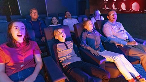 Group of children and adults enjoying a 3D movie experience at a cinema, with 3D glasses and excited expressions.