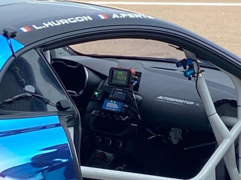Close-up of a race car cockpit featuring racing gear and digital displays, highlighting Grand Prix Racewear's professional racing equipment.