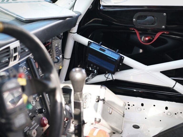 Close-up of a race car interior showing a digital dashboard, gear shifter, and safety roll cage for Grand Prix Racewear.