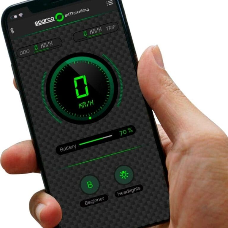 Close-up of a hand holding a smartphone displaying the Sparco mobility app with speed, trip, and battery info.