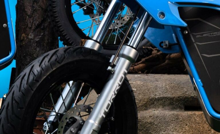 Close-up of a blue electric motorcycle with front suspension and knobby tyre, showcasing Grand Prix Racewear gear for motocross enthusiasts.