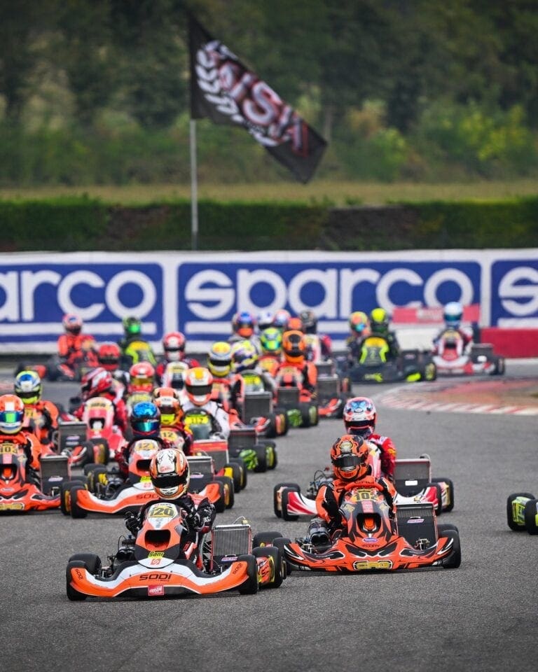 Grand Prix Racewear kart racing event with multiple drivers in colourful suits and helmets on a race track.
