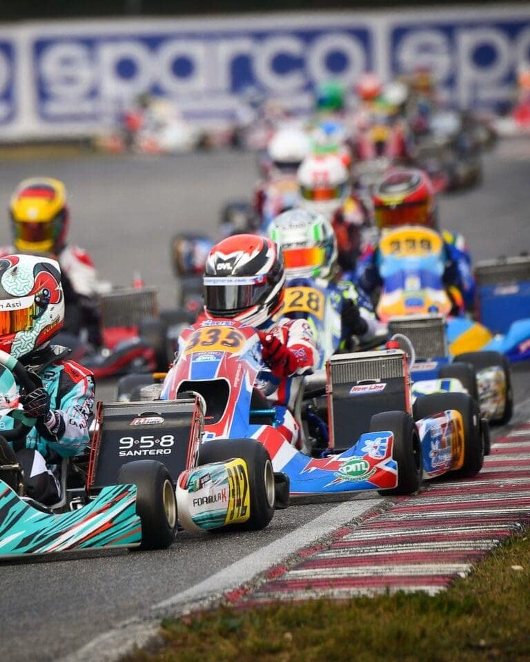 Close-up of go-kart racers competing on a track with a crowded background of other racers and banners.
