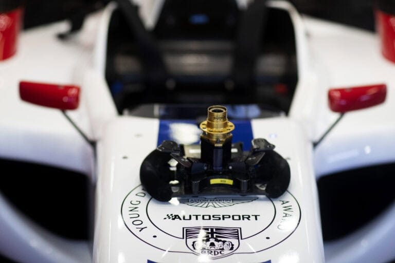 Close-up of a racing car's steering wheel and dashboard with detailed controls and branding, showcasing Grand Prix Racewear equipment.
