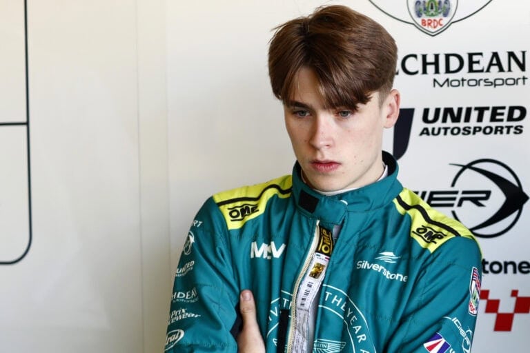 Young race car driver in blue racing suit with sponsor logos, preparing for a race at Grand Prix Racewear.