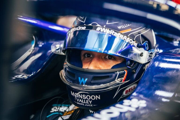 Close-up of a race car driver wearing a Bell helmet and racing suit, ready for a Grand Prix race, with focus on safety gear and helmet visor options.