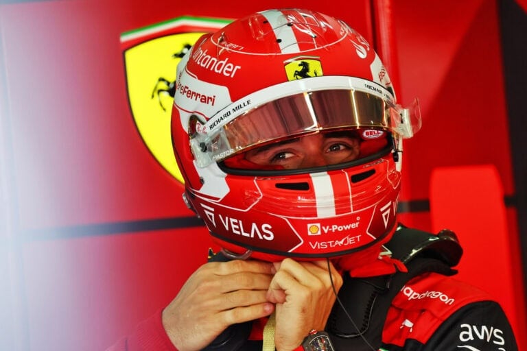 Close-up of a Ferrari Formula 1 driver wearing a red helmet with sponsor logos, preparing for a race.