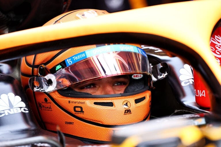Close-up of a Formula 1 driver wearing a yellow helmet with a tinted visor, seated in a race car, ready for a race.