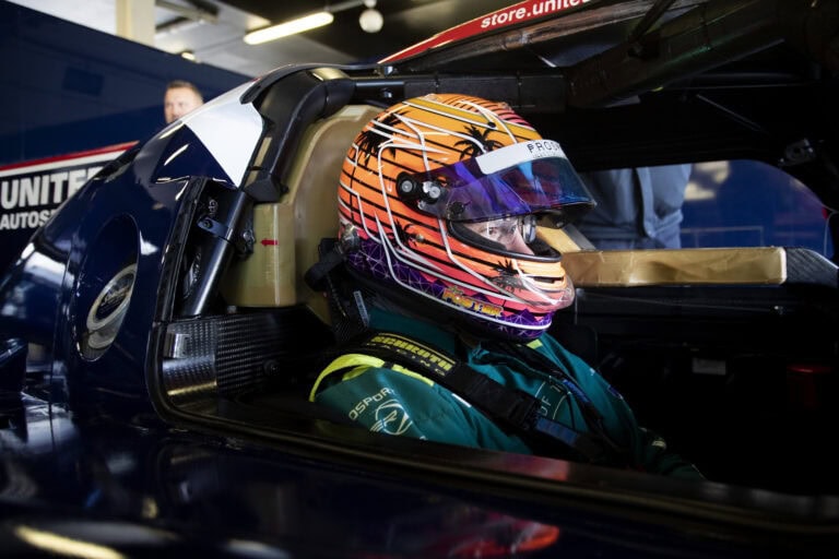 Close-up of a race car driver wearing a colourful helmet seated in a race car at a track day event.