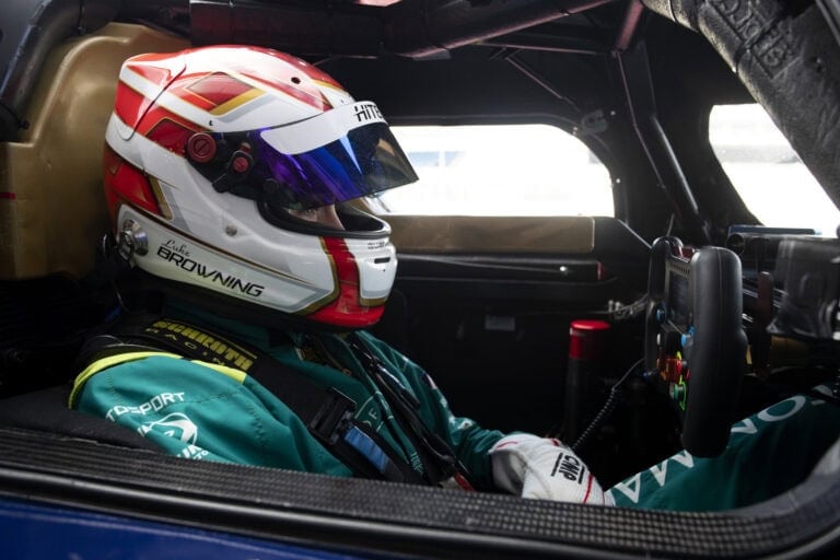 Race car driver wearing Grand Prix Racewear helmet and suit inside a racing car cockpit.