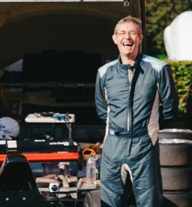 Smiling man in racing suit at motorsport event during National Motorsport Week.