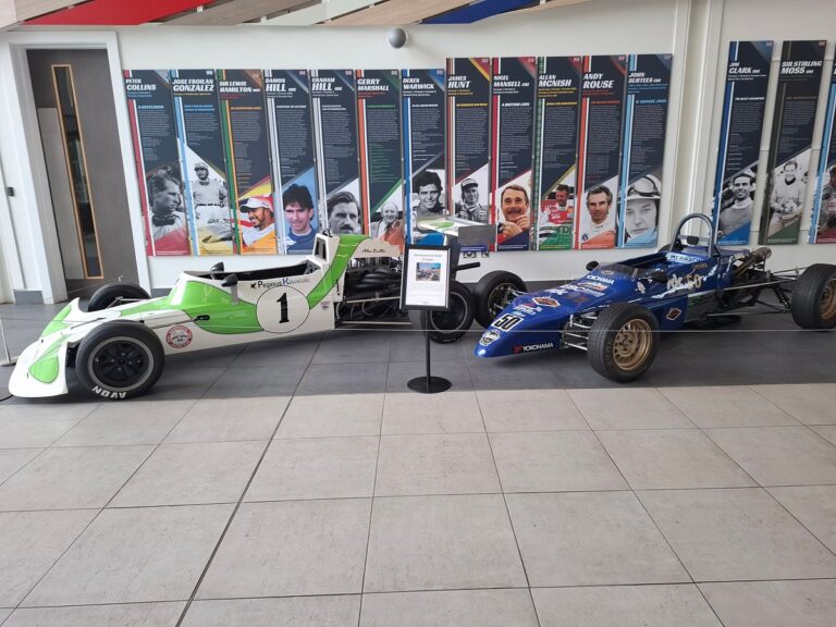 Two vintage Formula 1 race cars displayed at Silverstone Heritage Museum with historical driver profiles in the background.