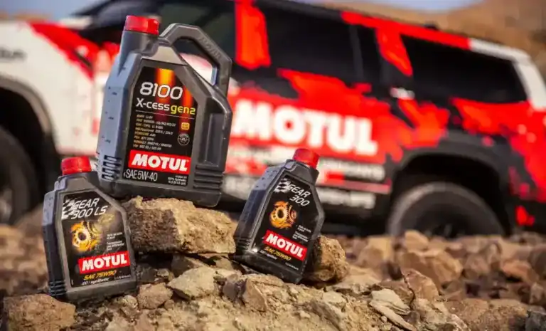 Motul motor oils displayed outdoors with a Motul vehicle in the background, highlighting high-performance lubricants for motorsport.