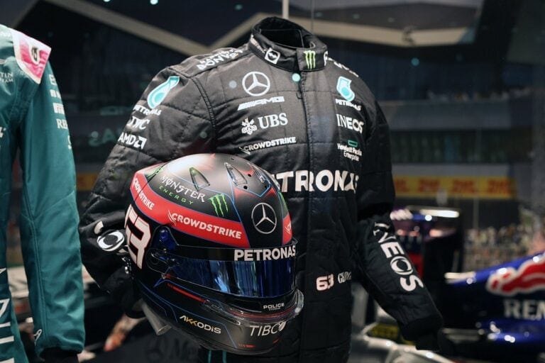 Formula 1 driver in racing suit holding a helmet at Silverstone Circuit, showcasing Grand Prix Racewear gear.