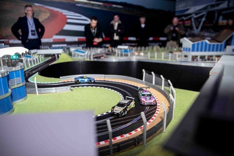 Detailed view of a slot car racing track with miniature race cars and spectators in the background.