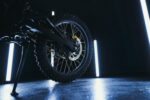 Close-up of a mountain bike's rear wheel and disc brake system in a dark setting with neon lighting.