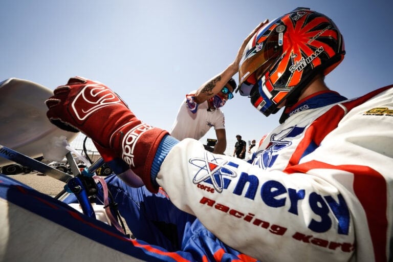 Racing driver wearing Grand Prix Racewear gloves and helmet, preparing for a race in a high-speed motorsport event.