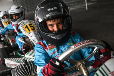 Young kart racer in full gear, smiling behind the helmet, ready for a race at Grand Prix Racewear.
