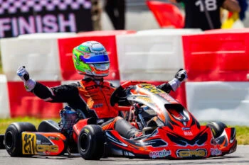 Kart racer celebrating victory at the finish line wearing Grand Prix Racewear, with a red and black go-kart and a colourful helmet.