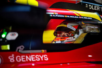 Close-up of a race car driver in a helmet inside a Formula 2 car, ready for a race, with focus on safety gear and racing environment.