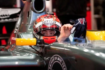 Young race car driver wearing a helmet and racing suit inside a Formula racing car, ready for a race.