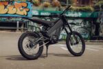 Electric mountain bike with full suspension and knobby tyres at an urban skatepark.