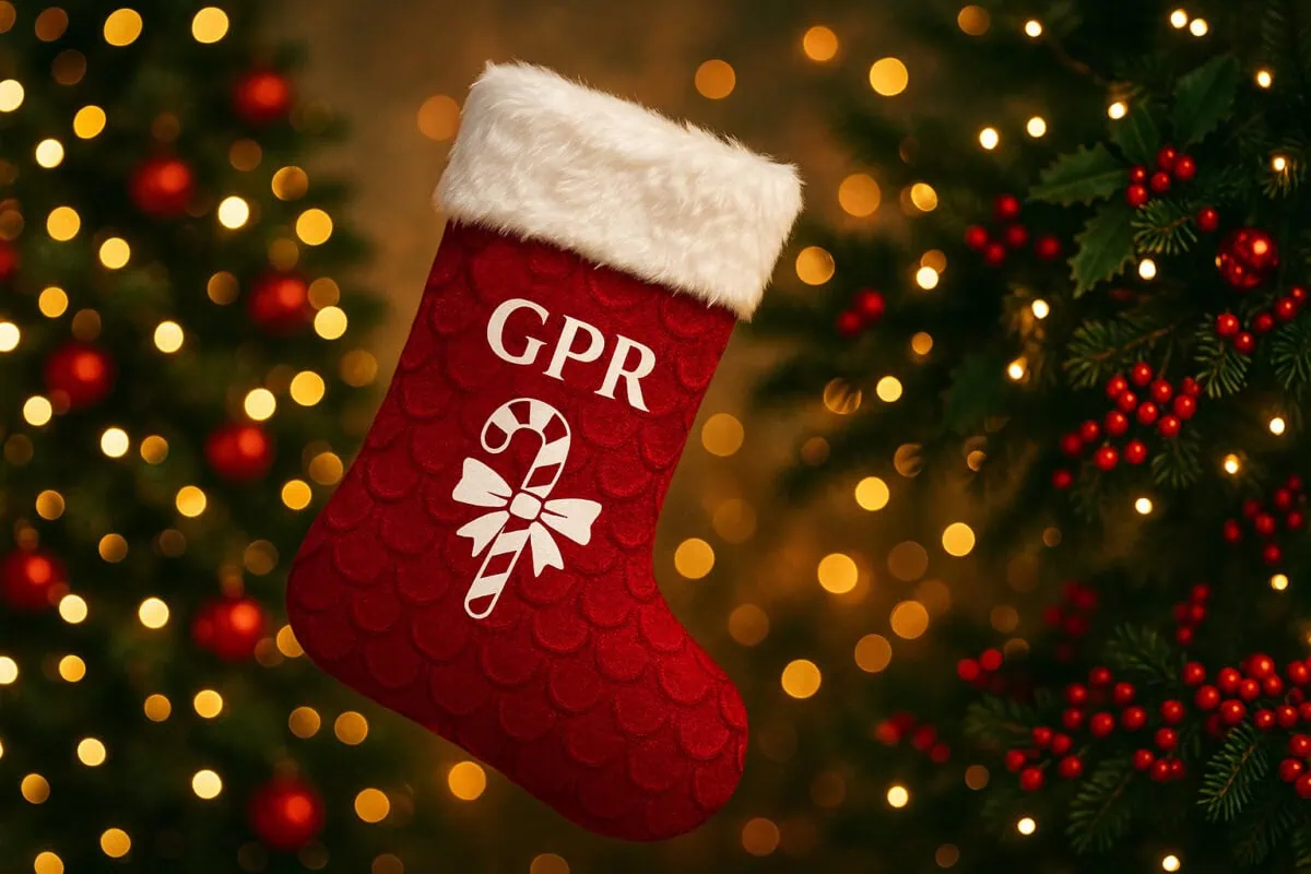 Festive Christmas stocking with 'GPR' initials and candy cane design hanging in front of decorated Christmas tree with lights and red berries.