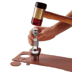 Close-up of a person using a hammer and a punch tool on a metal plate, demonstrating precision work in a workshop setting.