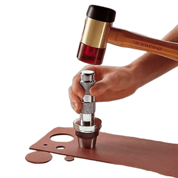 Close-up of a person using a hammer and a punch tool on a metal plate, demonstrating precision work in a workshop setting.