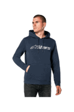 Man wearing a navy blue Grand Prix Racewear hoodie with Alpinestars logo, standing with hands in pockets, looking to the side.