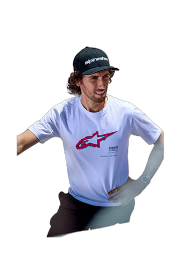 Young male motocross rider wearing Alpinestars cap and T-shirt, smiling confidently, representing Grand Prix Racewear for motorsport enthusiasts.