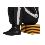 Close-up of racing gear including black racing shoes, black and white racing suit, and a yellow and black striped box, used for motorsport events.