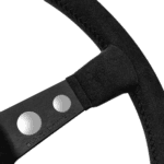 Close-up of a black racing steering wheel with metal spokes and textured grip, designed for high-performance motorsport use.