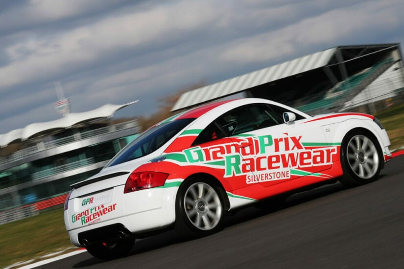 White race car with Grand Prix Racewear branding on a racetrack, speeding past the Silverstone circuit.
