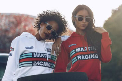 Two women wearing Grand Prix Racewear hoodies with racing stripes and sunglasses, posing outdoors for a promotional image.