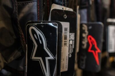 Close-up of racing helmet tags featuring the iconic Alpinestars logo in black and red, displayed at a motorsport store.
